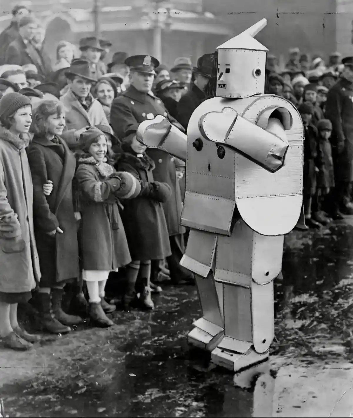 A black-and-white historical photo shows a person in a homemade, riveted tin robot costume standing before a crowd of…