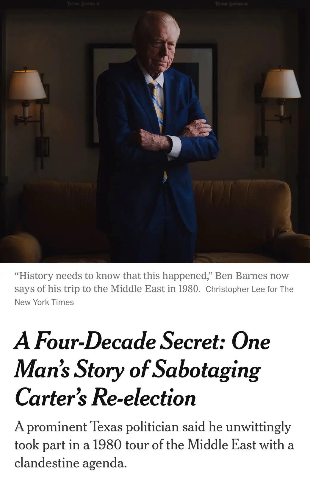 The image shows an older man in a blue suit and yellow tie standing with arms crossed in a dimly lit room with a couch and…