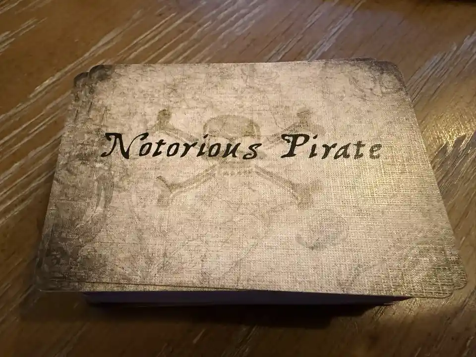A stack of playing cards with a weathered, parchment-like texture sits on a wooden surface. The top card features the text…