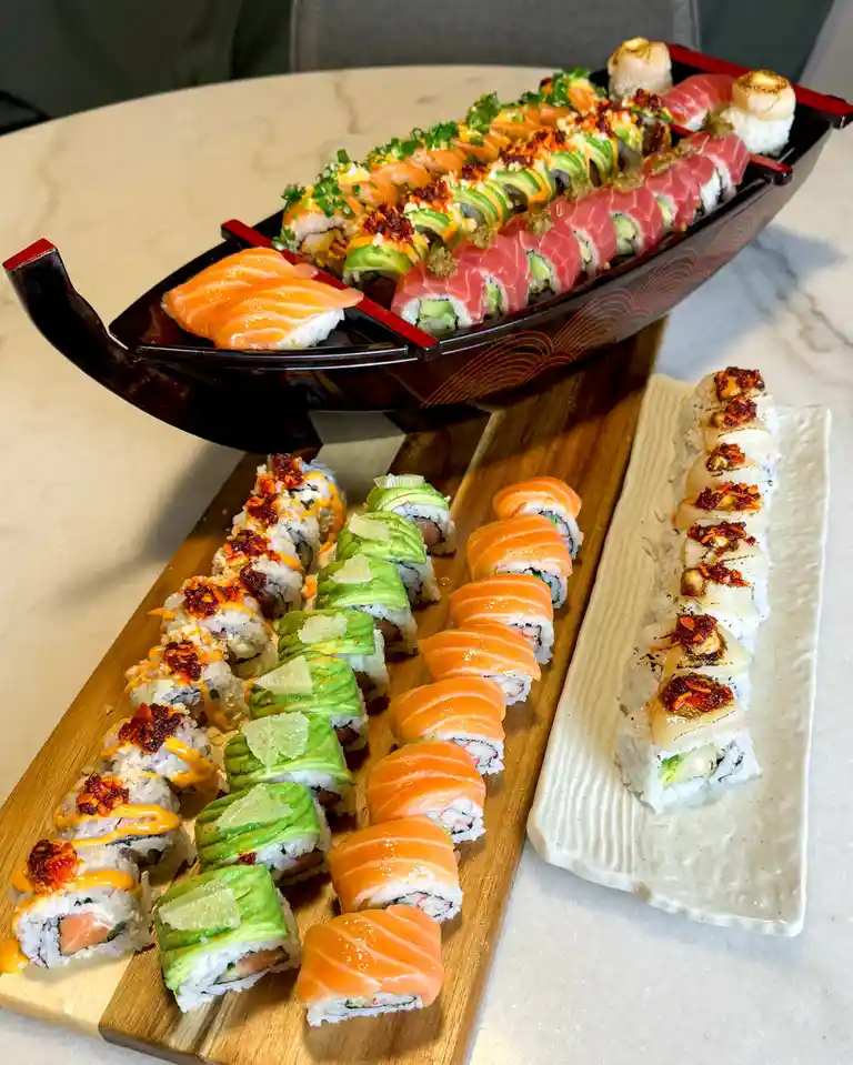 A lavish sushi platter is arranged to resemble a boat, with various rolls and sashimi displayed on a dark wooden boat-shaped…