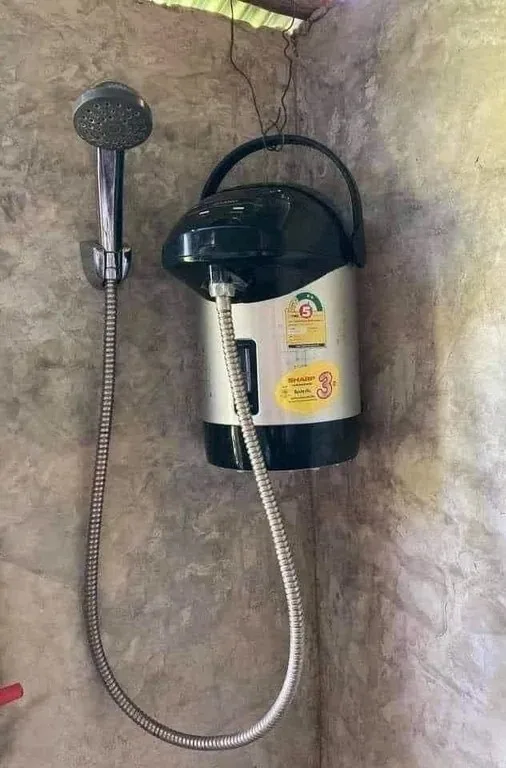 A showerhead is mounted on a wall next to a large, black and silver electric kettle with a handle, which is connected by a…