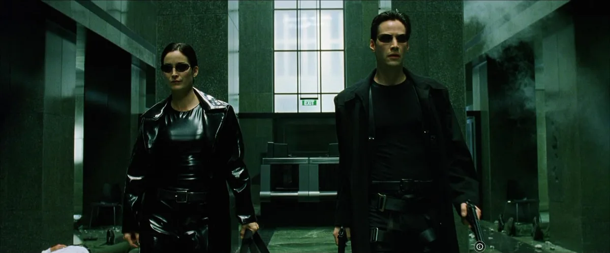 Two characters from 'The Matrix' (Neo and Trinity) stand in a dimly lit, smoke-filled hallway, both wearing black sunglasses…