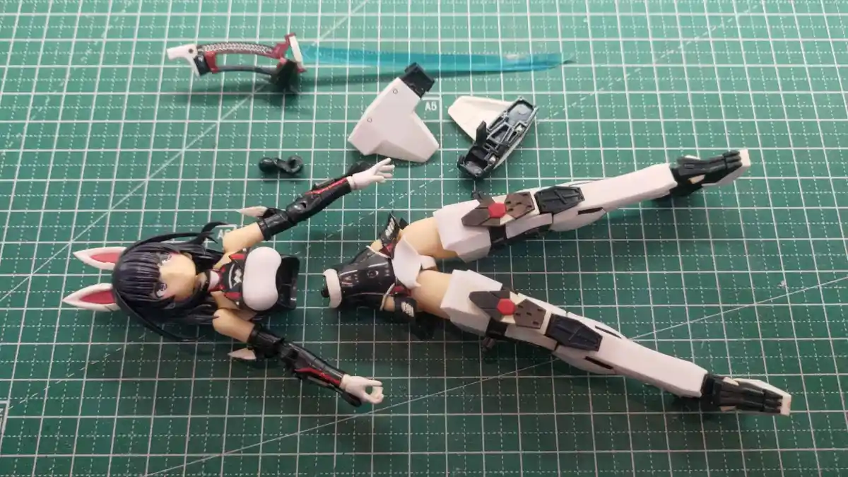 A disassembled anime-style action figure with bunny ears lies on a green cutting mat, surrounded by scattered plastic parts…