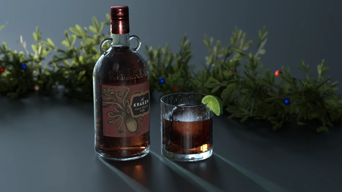 A bottle of The Kraken Gold Spiced Rum and a rocks glass with ice and a lime wedge sit on a dark surface, with a blurred…