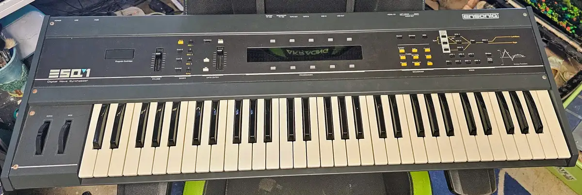 A top-down photo of a black Ensoniq ESQ-1 Digital Wave Synthesizer keyboard with cream and black keys, numerous knobs…