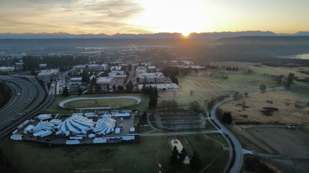 An aerial photo shows a sprawling landscape at sunset with mountains in the distance, a highway, and a large field with…