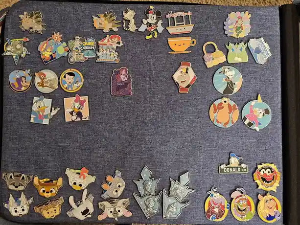 A collection of colorful Disney and Pixar character pins arranged on a blue fabric surface, with a pin featuring Donald Duck…