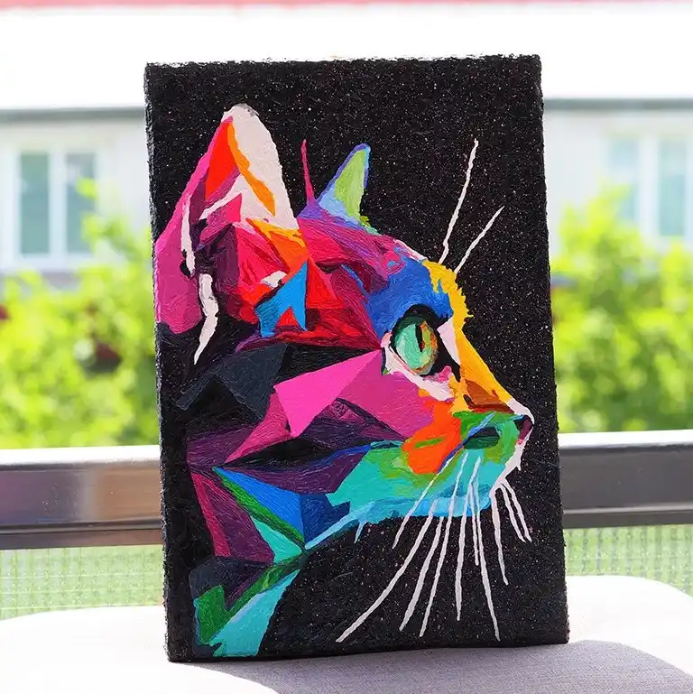 A colorful, geometric-style painting of a cat's head on a black textured canvas, featuring vibrant pink, blue, green, and…