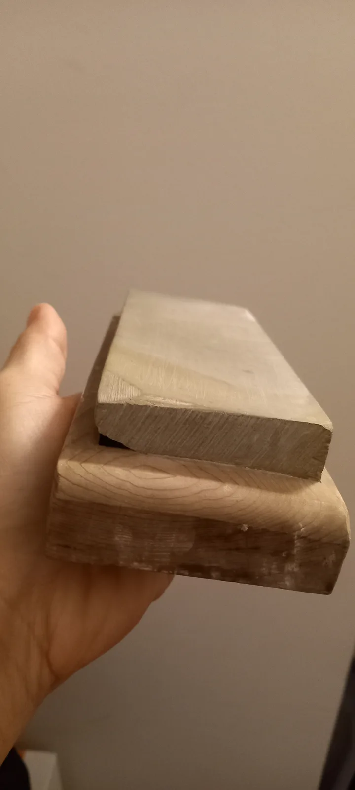 A hand holds two thick wooden blocks, one stacked atop the other, with the top block slightly askew. The image has no…
