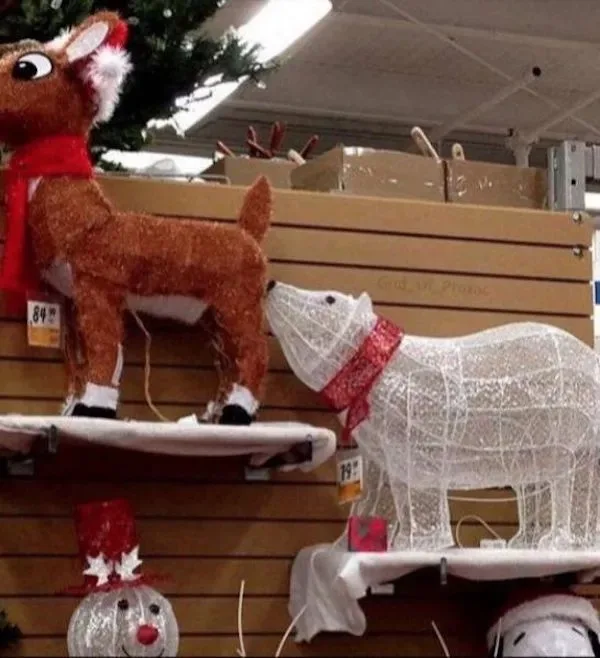 A white wireframe polar bear decoration with a red scarf is shown licking the rear of a brown, fuzzy reindeer decoration…