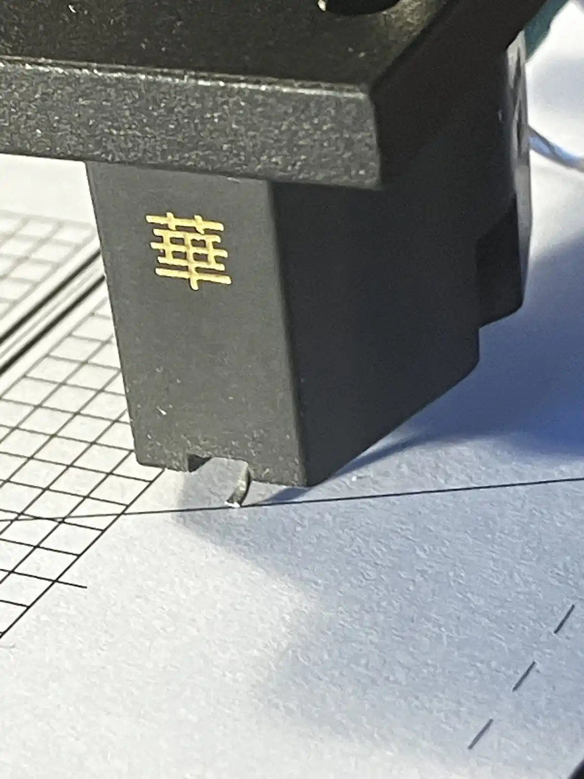 A close-up photo shows a black mechanical object, possibly a printer or electronic device, with a single golden Chinese…