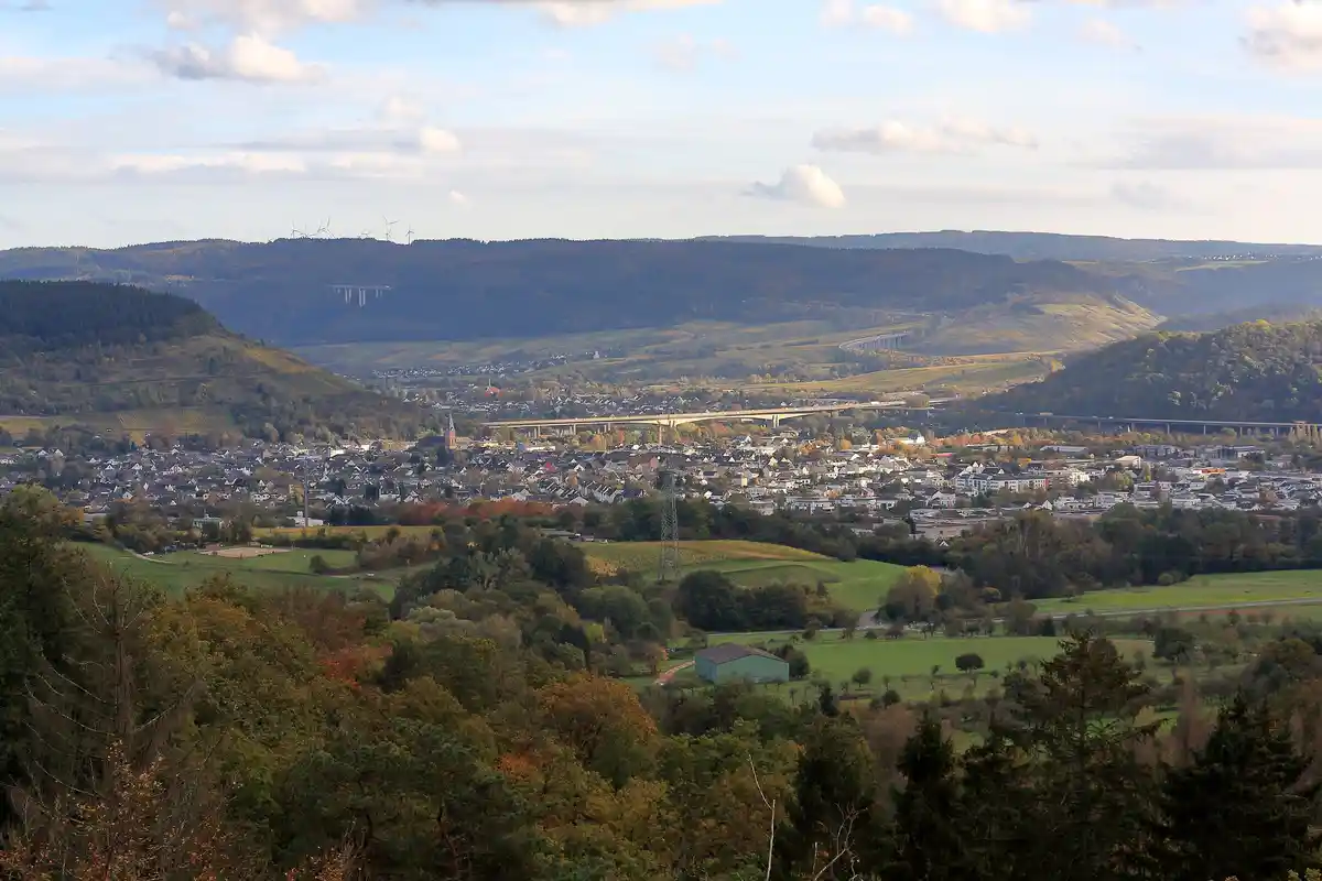 A scenic autumn landscape of rolling hills, forests, and a town with bridges and wind turbines, overlaid with the text 'i'm…