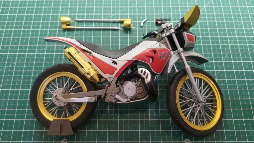 a detailed scale model of a red, white, and gold motorcycle sits on a green cutting mat, with several disassembled parts…