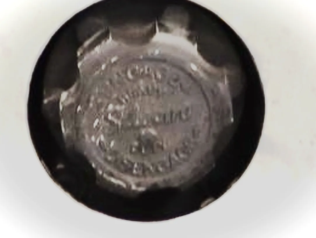 A blurry, close-up photo shows the bottom of a circular, metallic object with embossed text that is too indistinct to read…