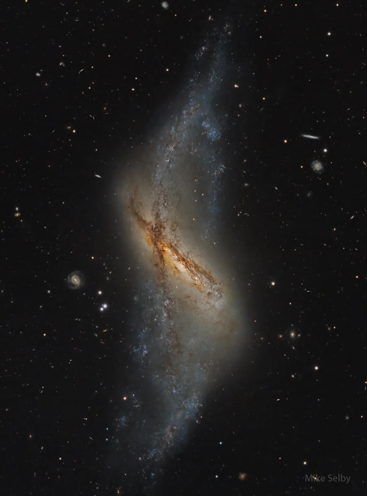 A deep-space photograph shows a spiral galaxy with a distinct, bright, diagonal band of stars and dust stretching across the…
