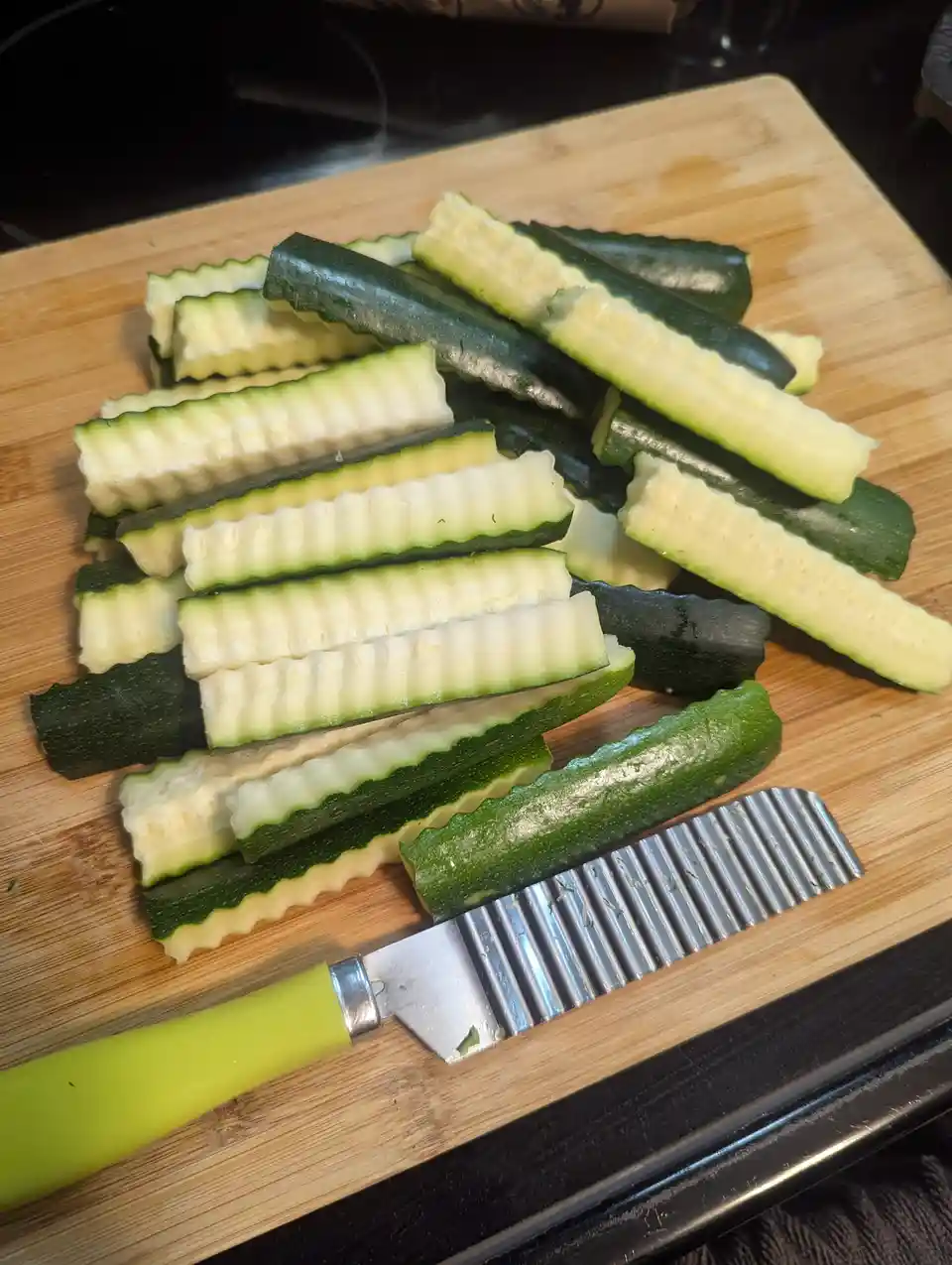 A wooden cutting board holds numerous green zucchini slices that have been cut into noodle-like strips using a ridged…