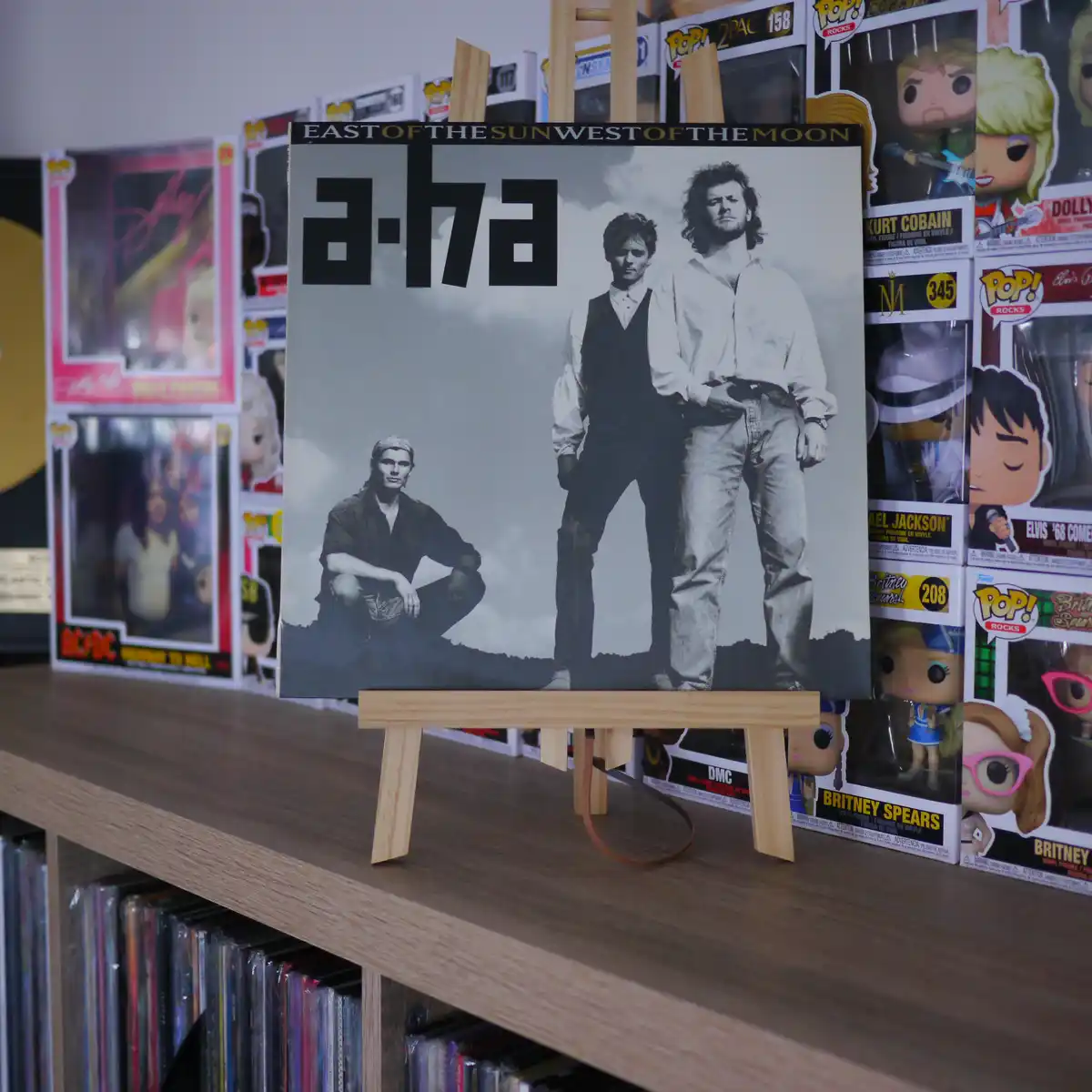 A black-and-white album cover of the band a-ha for their album 'East of the Sun West of the Moon' is displayed on a small…