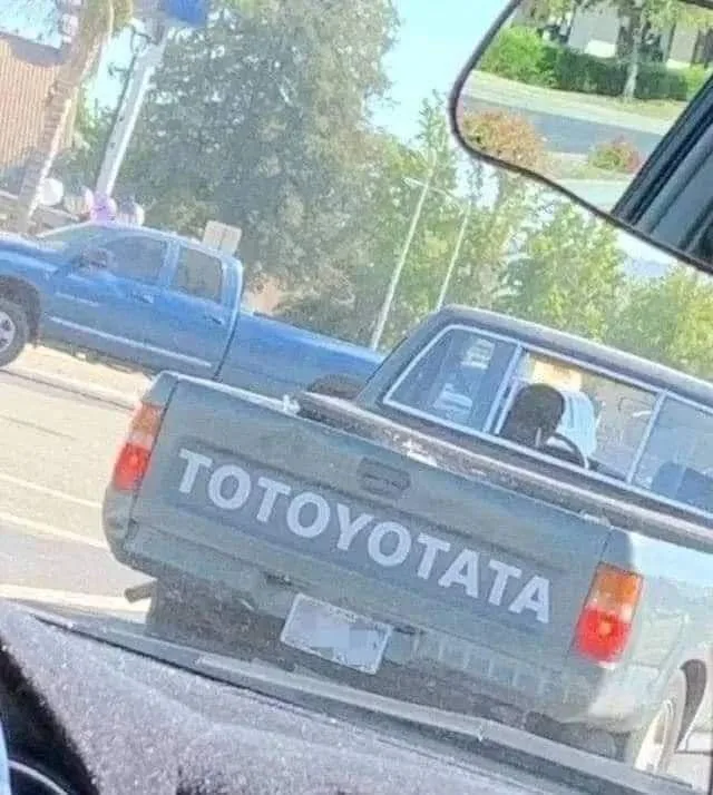 A blurry photo taken from inside a car shows the rear of a gray pickup truck with the word 'TOTOYOTATA' written in large…