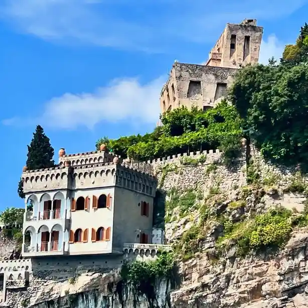 a picturesque view of a cliffside villa with arched windows and red shutters, perched above a rocky outcrop, with a…