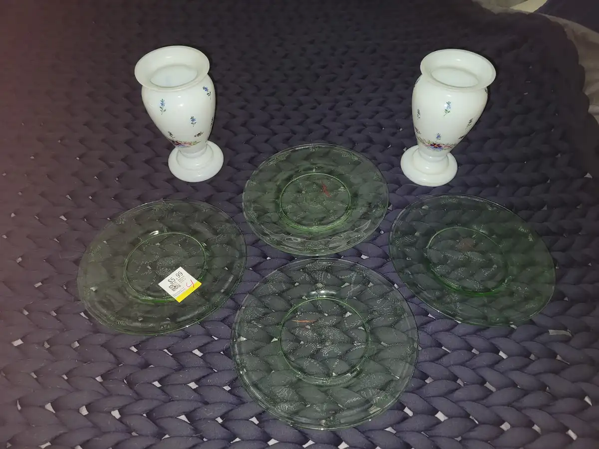 Four green glass plates with a textured pattern and two white ceramic vases with floral designs are arranged on a dark…