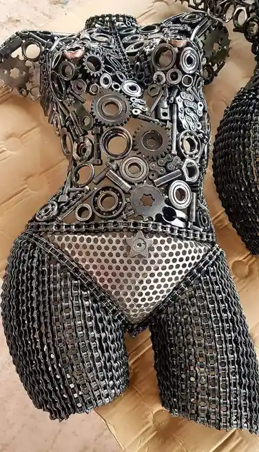A sculpture shaped like a human torso and hips, constructed entirely from repurposed mechanical parts including gears…