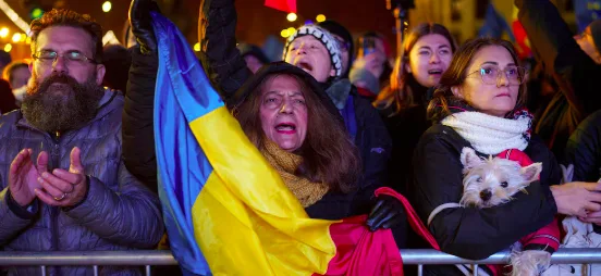 A crowd of people, including a woman holding a Ukrainian flag and another holding a small dog, are visibly emotional and…