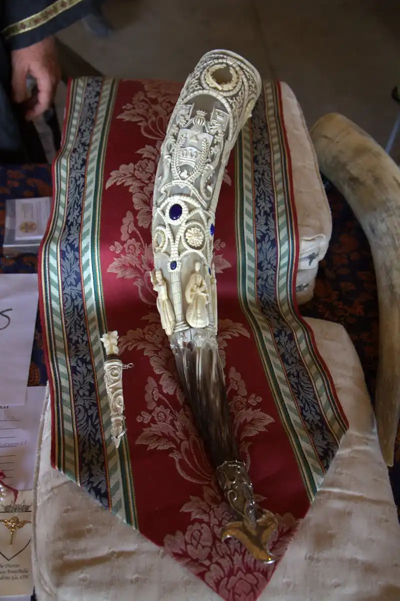 a highly ornate, intricately carved ceremonial horn with embedded blue stones and detailed carvings rests on a rich red and…