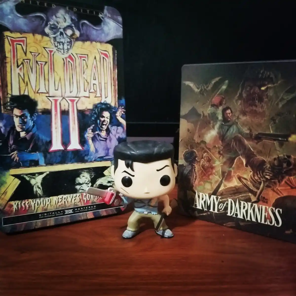 A Funko Pop! figure of Ash Williams from 'Army of Darkness' stands between two movie steelbook cases: 'Evil Dead II' on the…