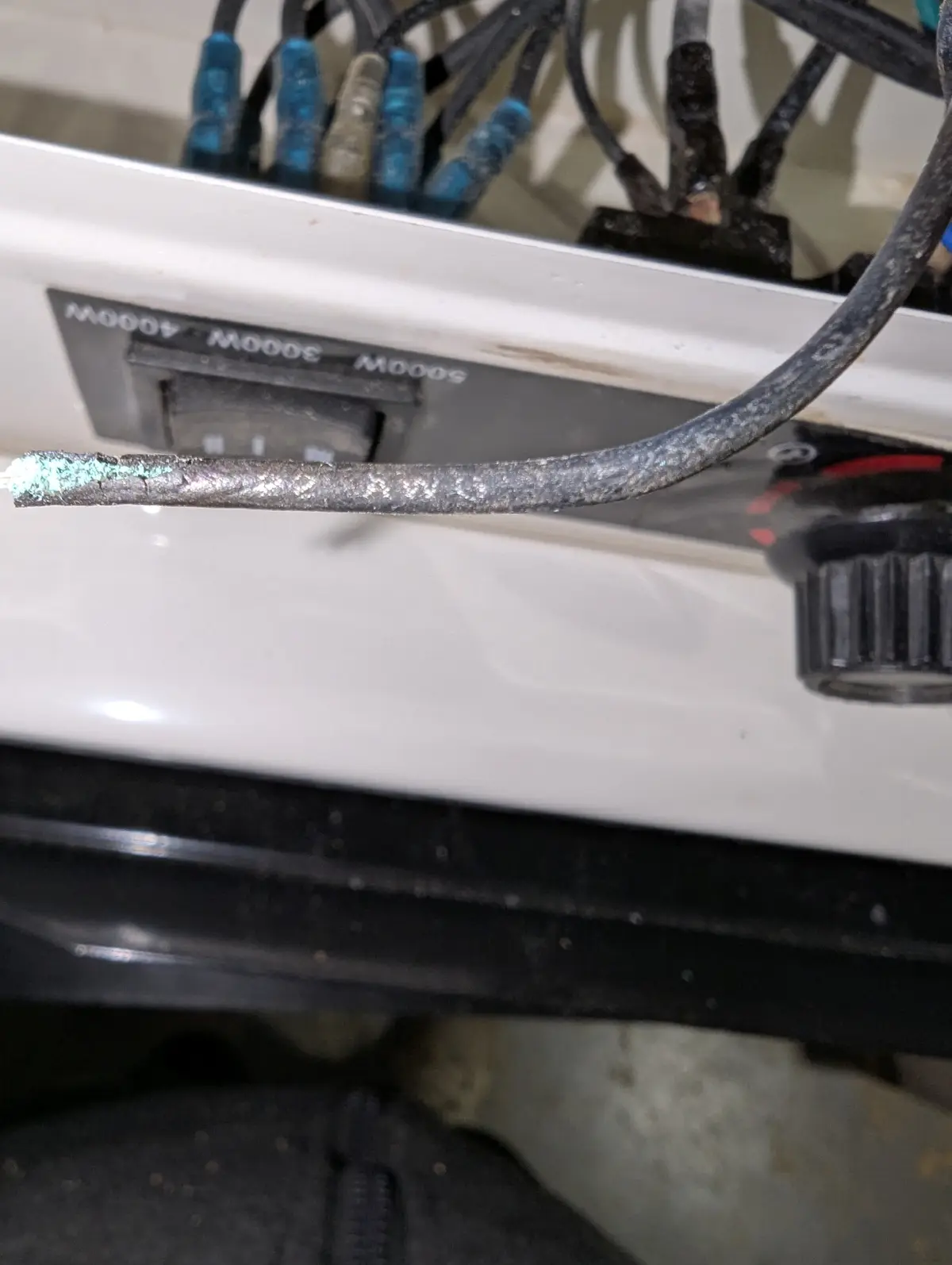 A close-up photo shows a severely damaged, frayed, and corroded electrical wire protruding from a white appliance, likely a…