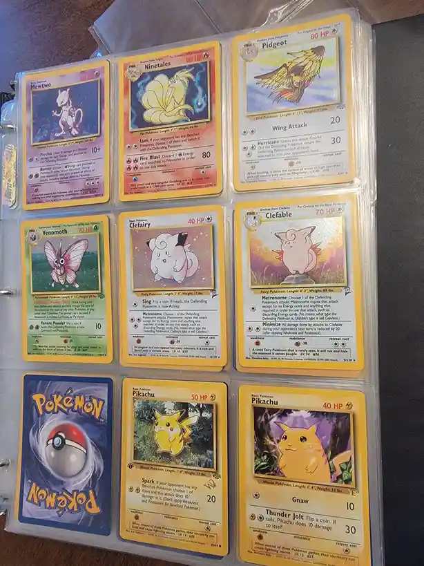 A collection of Pokémon trading cards from the 1999 Base Set, displayed in a binder. The cards include Mewtwo, Ninetales…