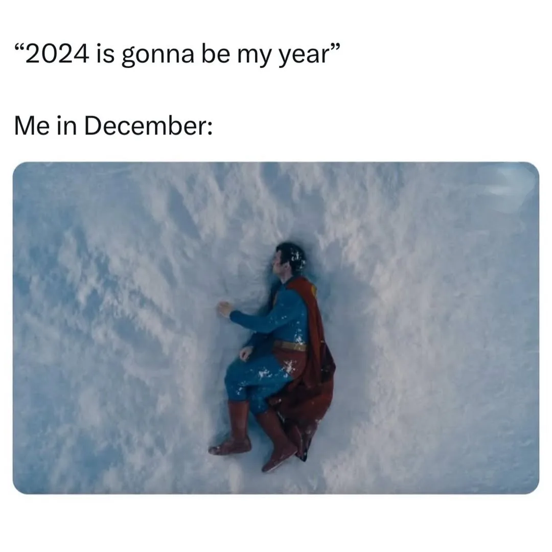 An overhead shot shows a man in a blue and red superhero costume, covered in snow, sitting defeated in a snowy landscape…