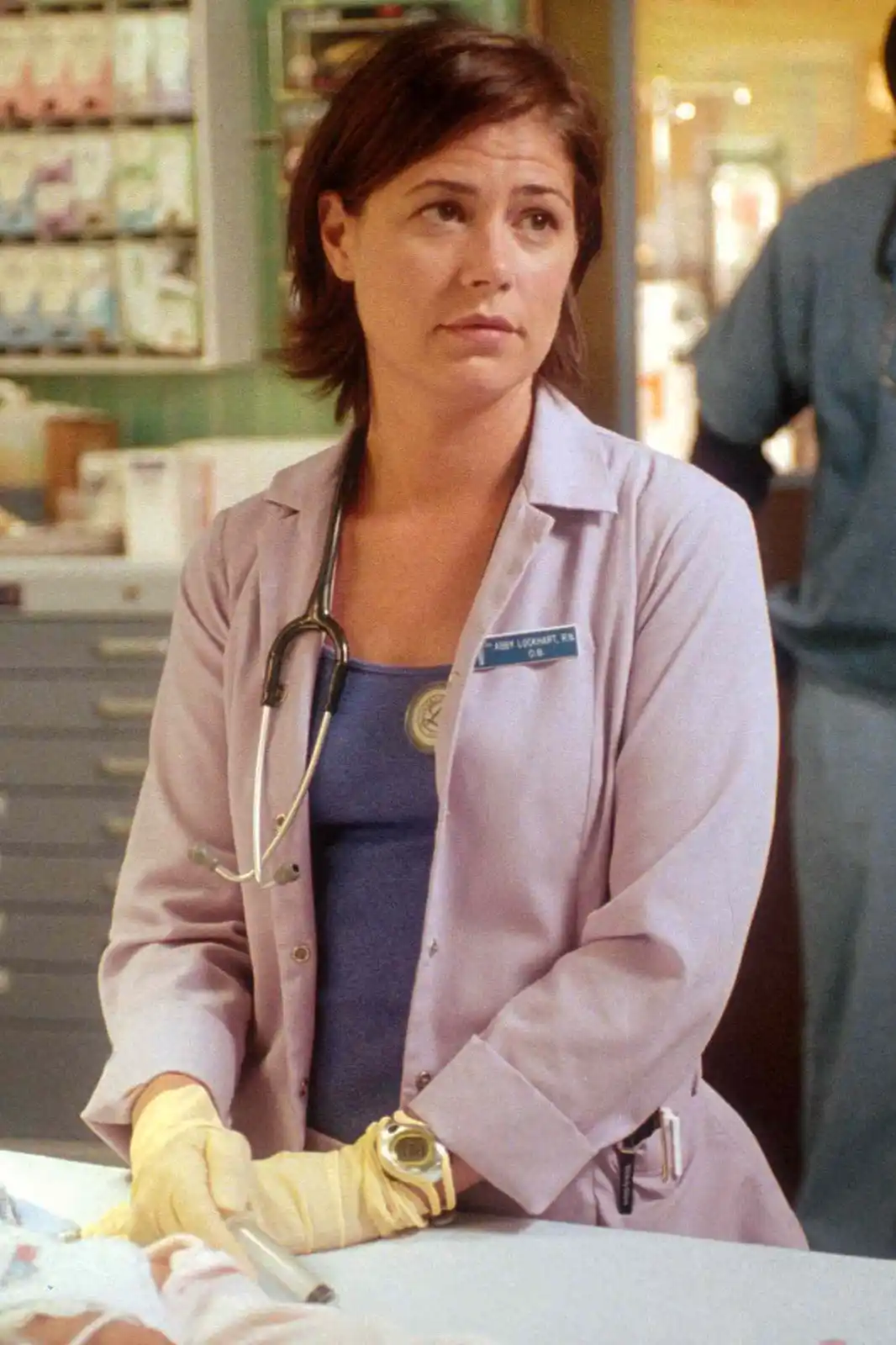 A woman in a light purple medical coat with a stethoscope around her neck and yellow gloves looks upward with a skeptical…