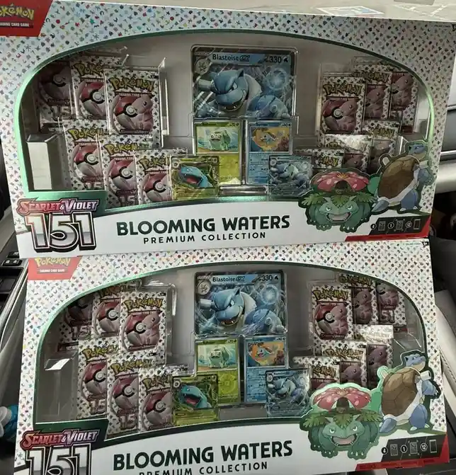 Two identical Pokémon Trading Card Game 'Scarlet & Violet 151 Blooming Waters Premium Collection' boxes are stacked, each…