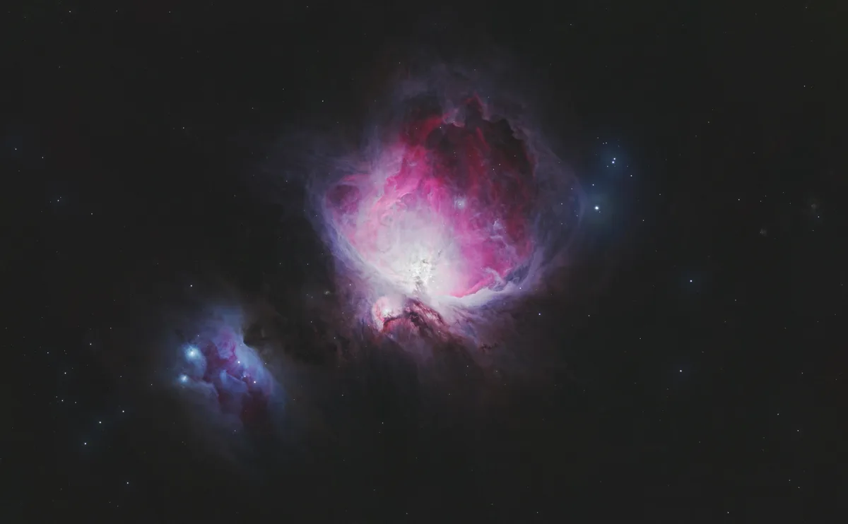 A stunning astrophotograph of the Orion Nebula, showcasing vibrant pink, red, and blue cosmic clouds against a black…