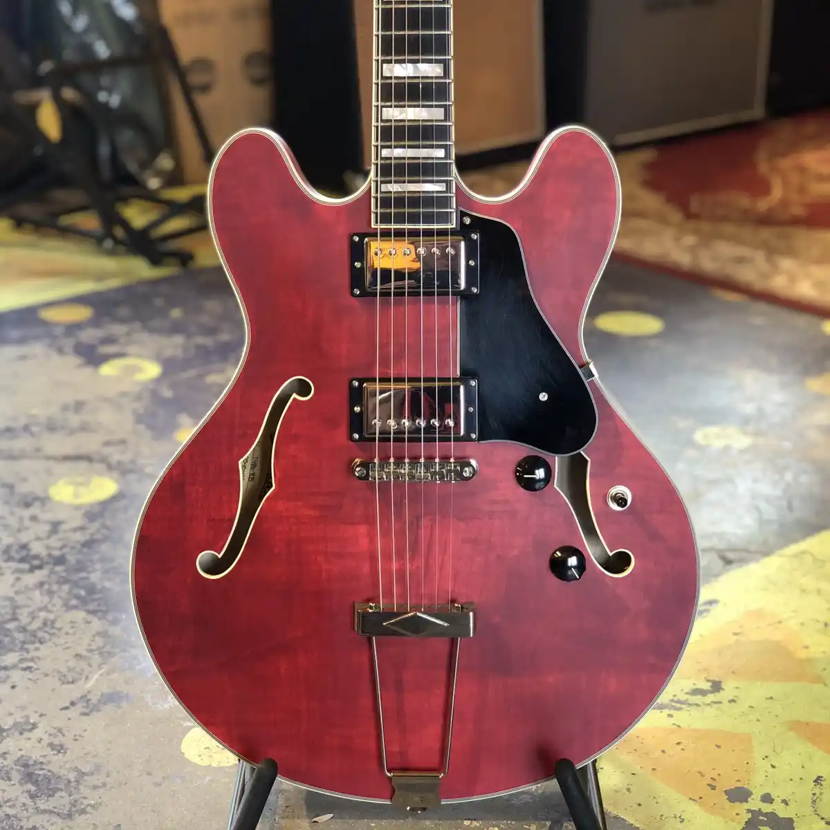 A close-up photo of a red semi-hollow body electric guitar with f-holes, chrome hardware, and a black pickguard, standing…