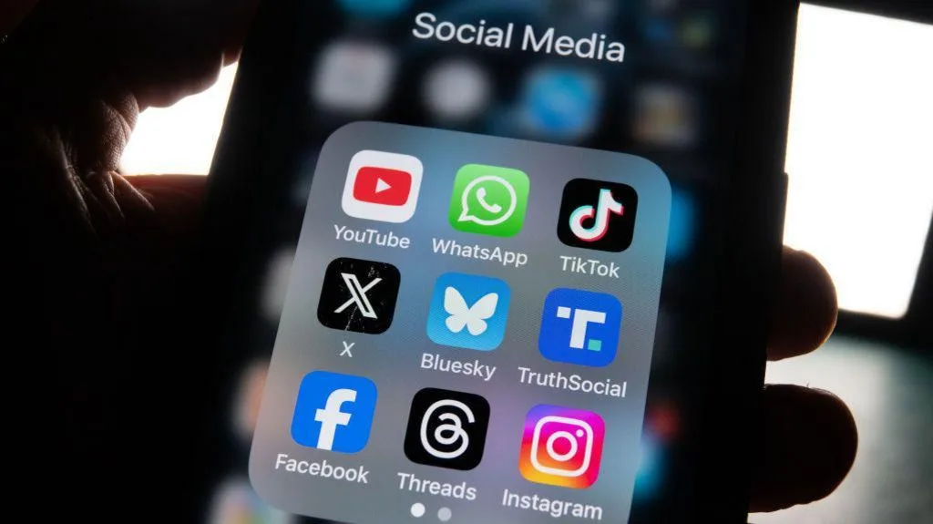 A close-up photo of a smartphone screen showing a folder labeled 'Social Media' containing app icons for YouTube, WhatsApp…