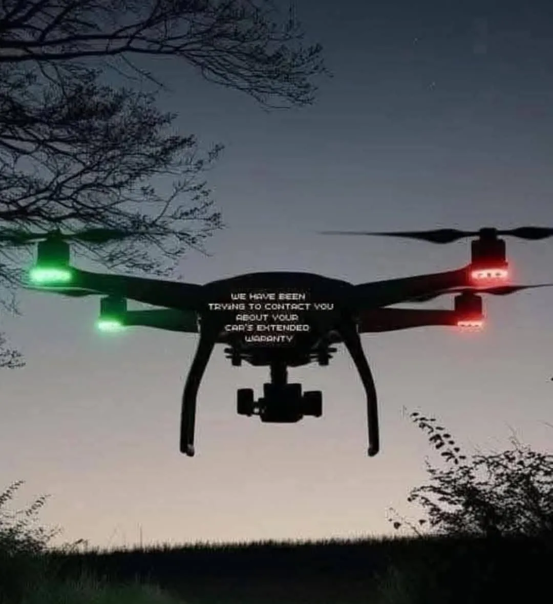 A drone is flying at dusk with green and red lights on its arms, silhouetted against a twilight sky with tree branches…