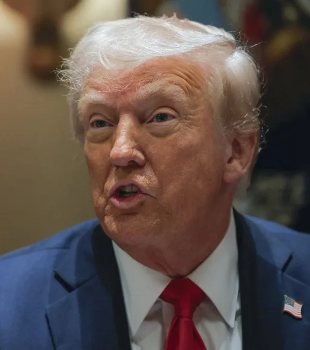 a close-up photo of former president donald trump, wearing a blue suit, white shirt, and red tie, with an american flag pin…