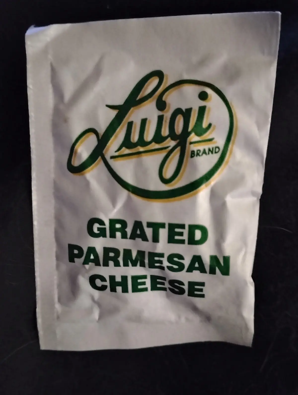 A crumpled white packet of grated parmesan cheese features a logo that reads 'Luigi Brand' in green cursive script with a…