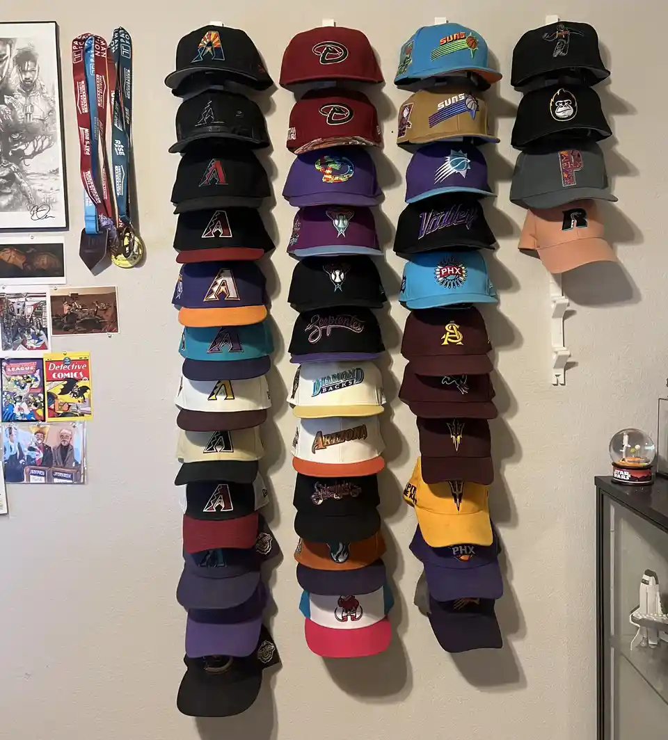 A wall displays four tall, vertical stacks of colorful baseball caps, mostly featuring Arizona Diamondbacks, Phoenix Suns…