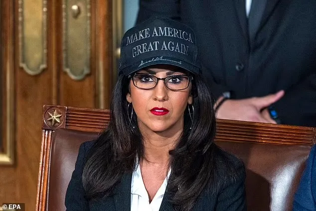 a woman with dark hair, glasses, and red lipstick sits in a wooden chair wearing a black baseball cap with the text 'MAKE…