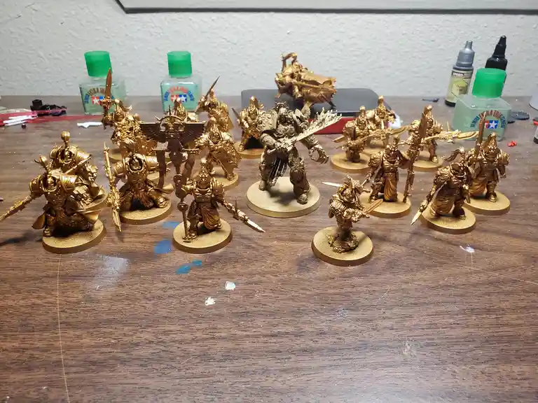 A collection of intricately detailed fantasy miniatures, all uniformly painted gold, are arranged on a wooden table…