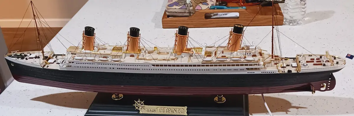 A detailed model of the RMS Titanic, featuring its iconic four funnels, white superstructure, and black hull, displayed on a…