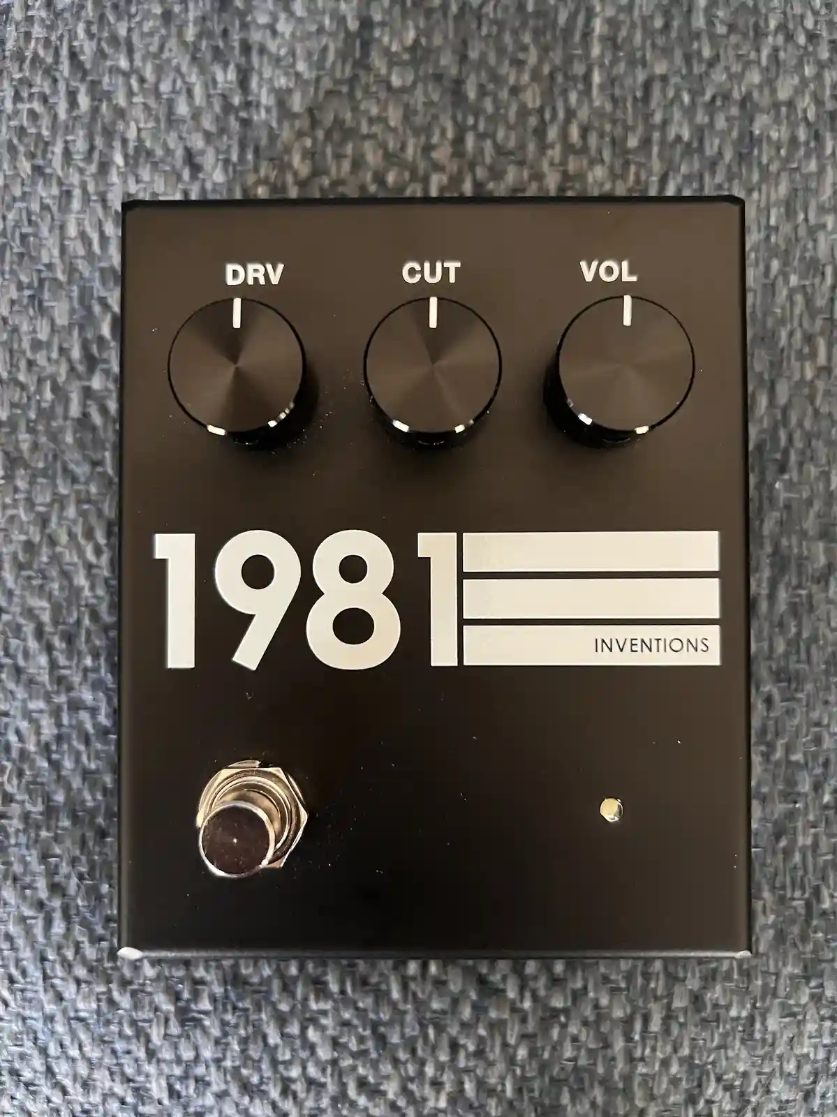 A black guitar effects pedal labeled '1981 INVENTIONS' with three knobs labeled DRV, CUT, and VOL, all set to minimum, and a…
