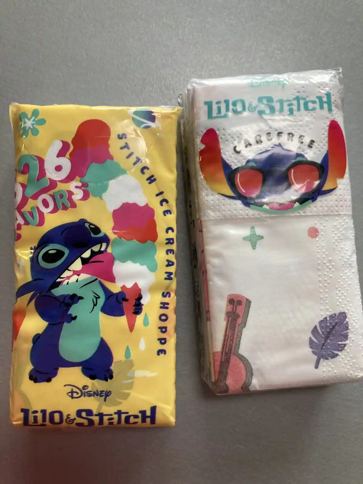 Two Disney Lilo & Stitch themed napkin packages sit side by side on a gray surface. The left package is yellow and features…