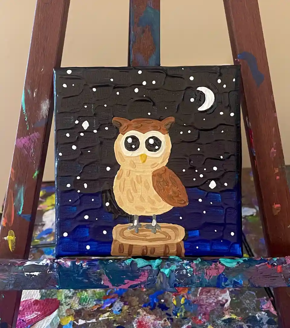 A small, textured painting on canvas depicts a cartoonish owl with large eyes perched on a tree stump against a night sky…