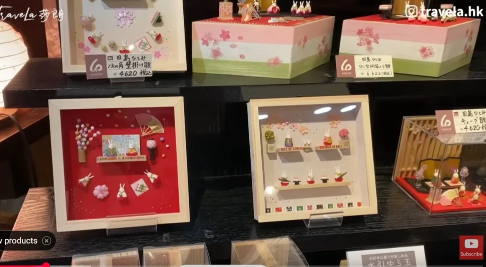 A display of Japanese decorative items, including framed shadow boxes with miniature origami rabbits, flowers, and fans, and…