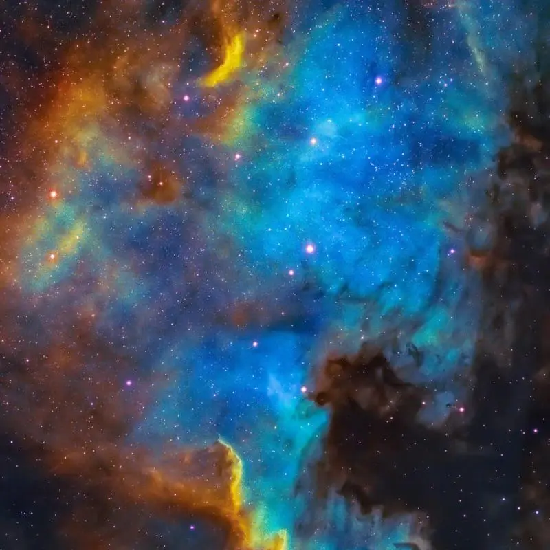 A vibrant cosmic nebula image with swirling blue, orange, and yellow clouds of gas and dust, dotted with countless stars…