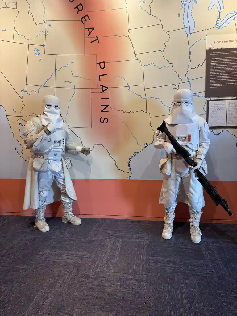 Two full-body Stormtrooper costumes stand side-by-side in front of a large map of the United States, with the region labeled…