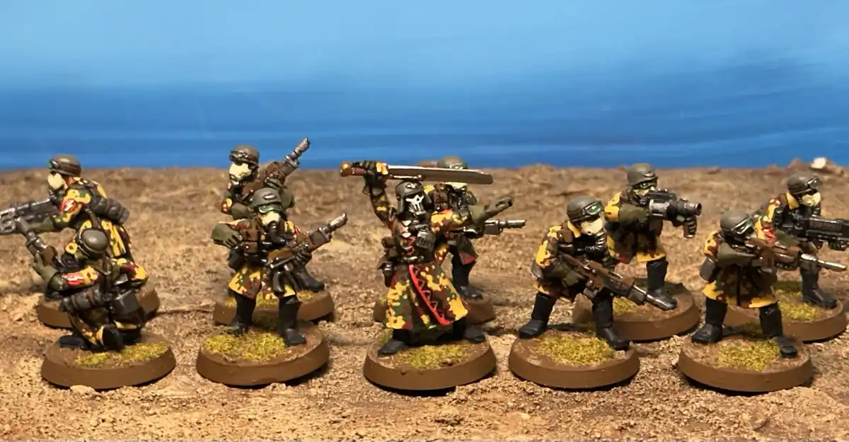 A row of painted miniature soldiers in desert camouflage gear, most holding firearms, with one central figure prominently…
